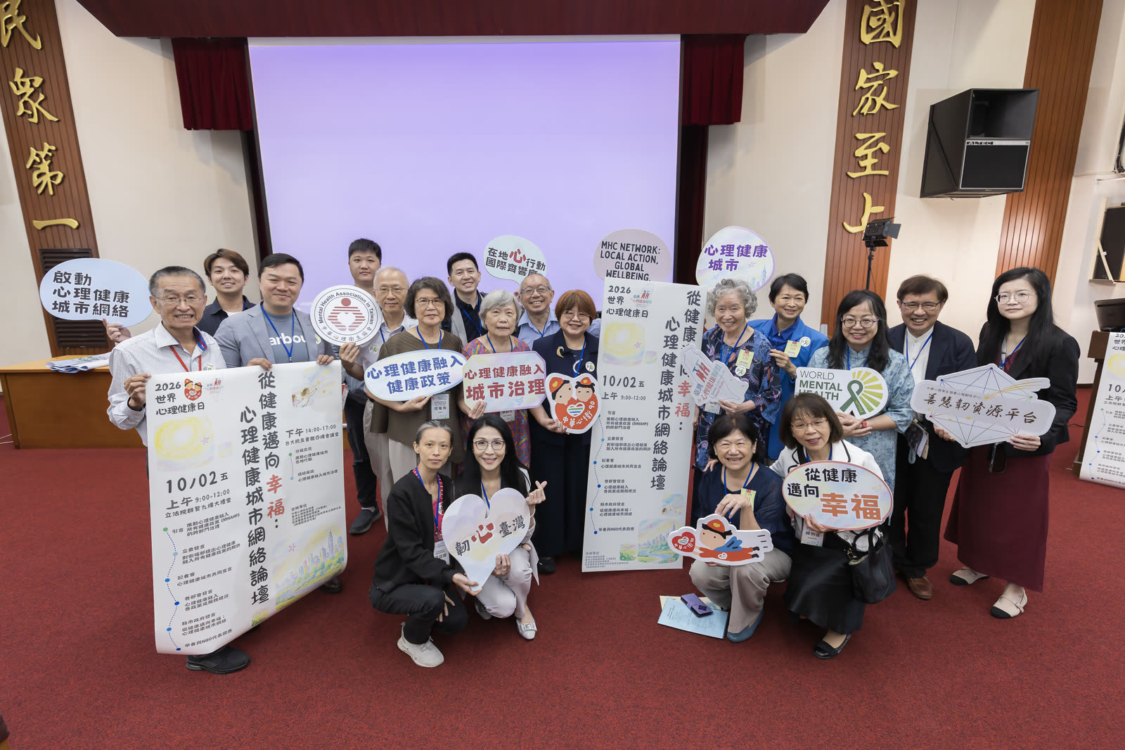 2026 年 10 月 2 日心理健康城市網絡論壇的盟友合照，與會者手持標語牌與議程海報合影