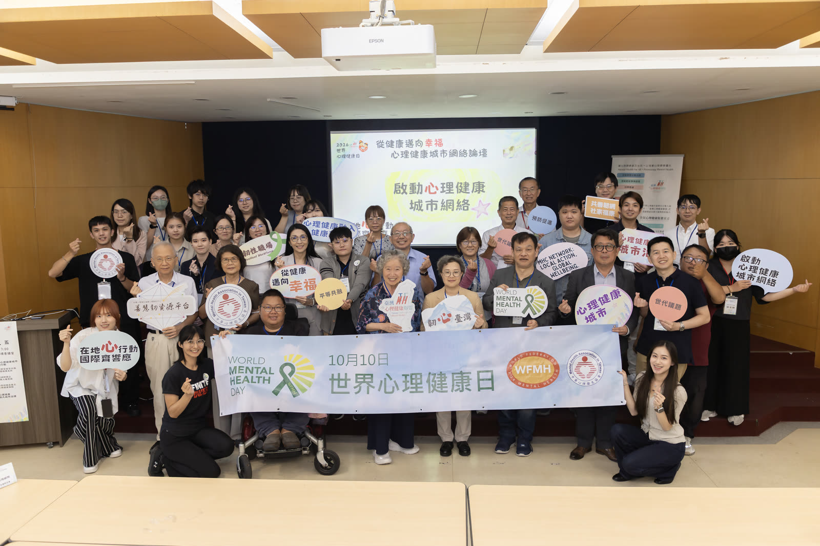 下午論壇結束時的大合照，與會者手持標語牌，後方投影幕顯示論壇標題